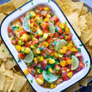 white bowl of peach salsa sitting on grey platter of tortilla chips