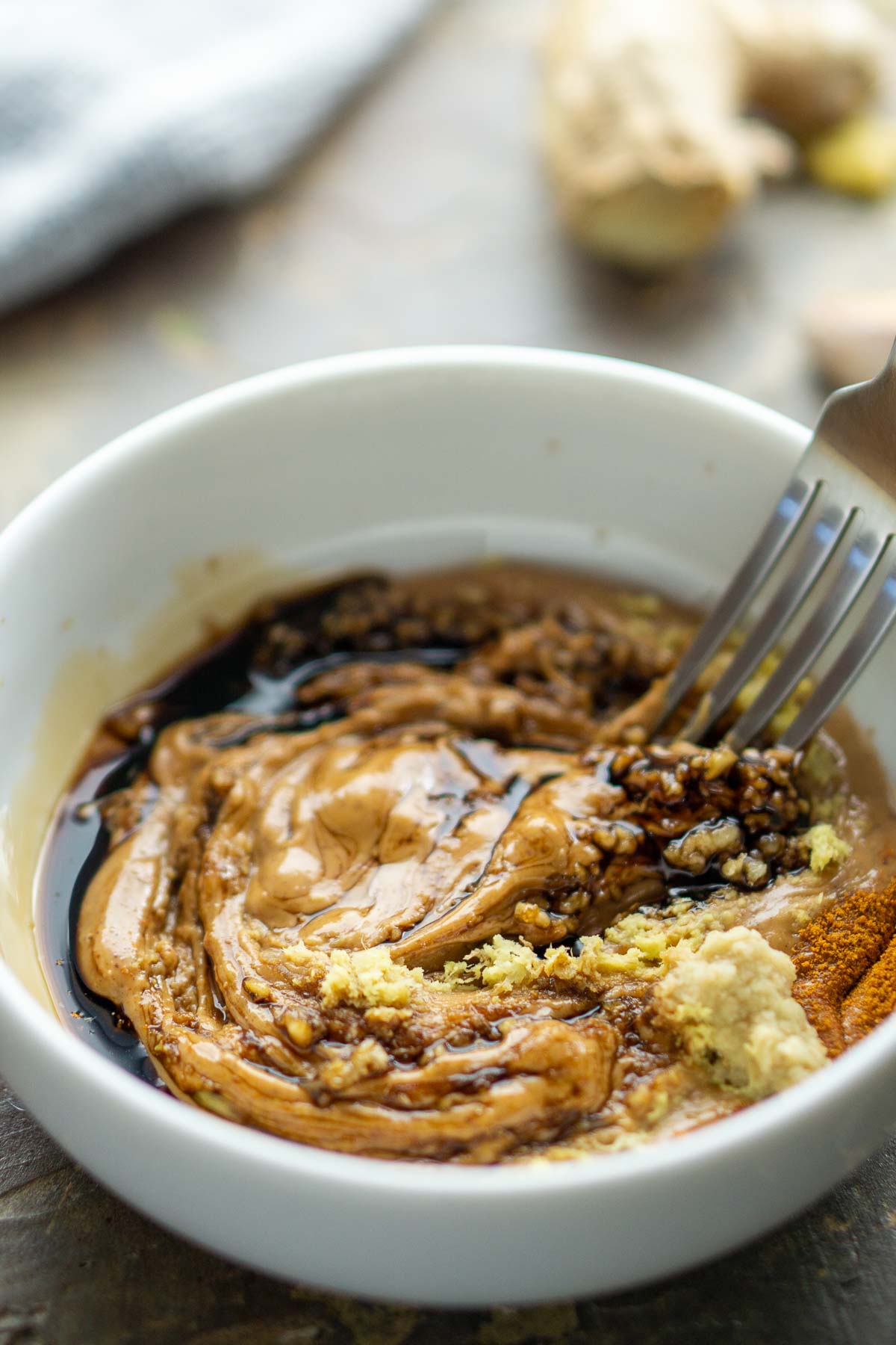 fork stirs peanut sauce ingredients in white bowl