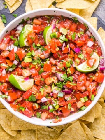 pico de gallo in white serving bowl surrounded by tortilla chips and serrano peppers