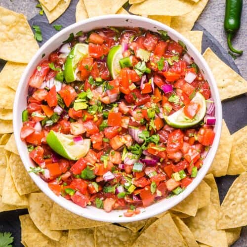 pico de gallo in white serving bowl surrounded by tortilla chips and serrano peppers