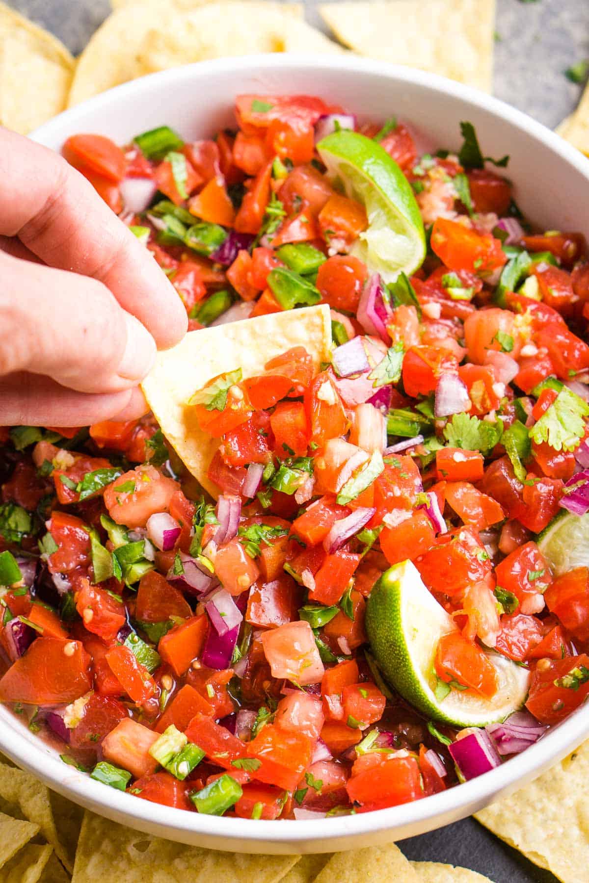 pico de gallo in white serving bowl being scooped by hand with tortilla chip