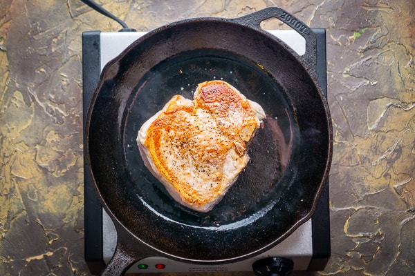 pan seared bone-in pork chop in cast iron skillet on electric burner