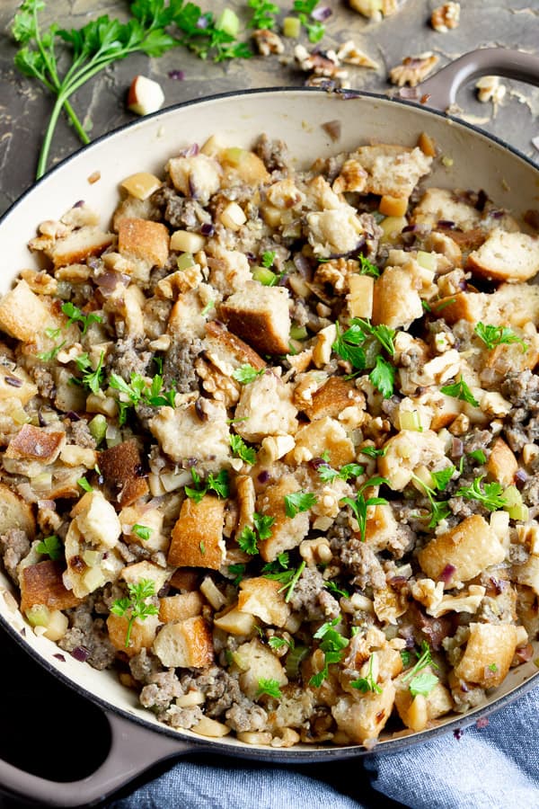 sausage stuffing in skillet with scattered parsley, walnuts, and blue linen