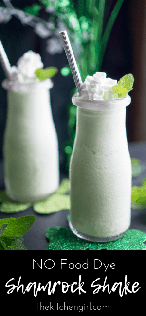 shamrock shake in glass bottles with straw, whipped cream, and mint leaf garnish next to St Patrick's Day decorations