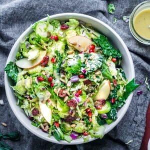 shaved Brussels sprout salad with kale, apples, dried cranberries, and pomegranate in a white bowl