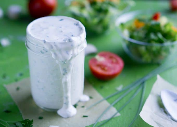 Greek yogurt ranch dressing in mason jar next to green salads and fresh tomatoes