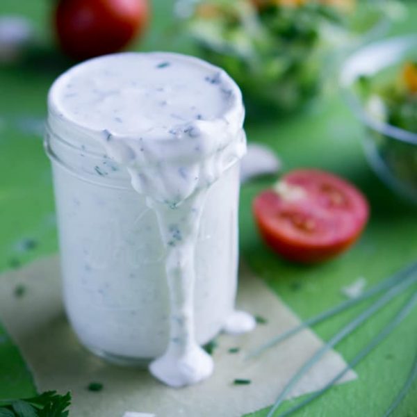 Greek yogurt ranch dressing in mason jar next to green salads and fresh tomatoes