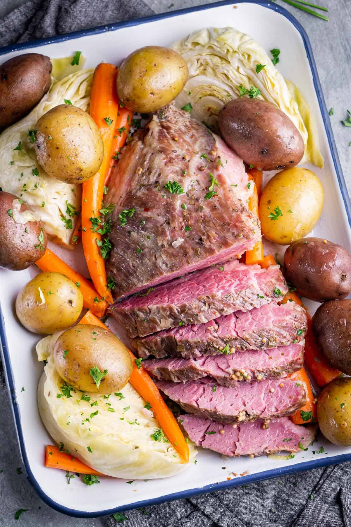 Sliced corned beef in roasting pan with cabbage wedges, carrots, and whole potatoes