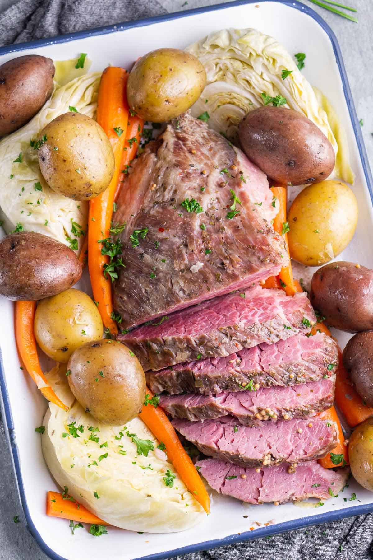 Sliced corned beef in pan, surrounded by whole potatoes, carrots, and cabbage