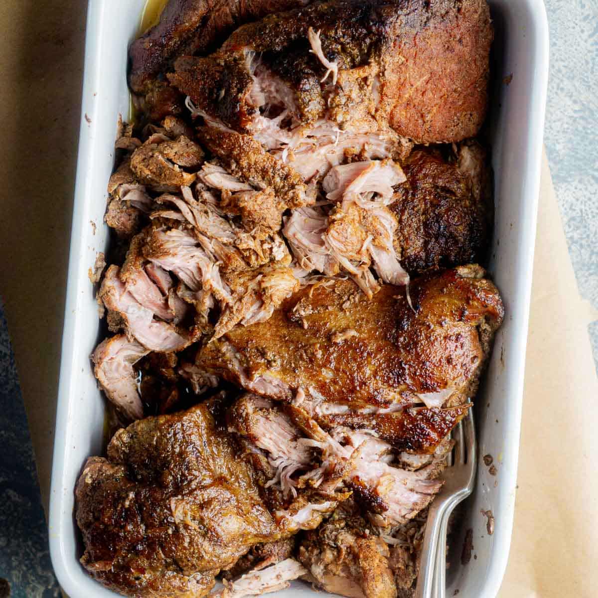 juicy shredded pulled pork in white serving dish with two forks