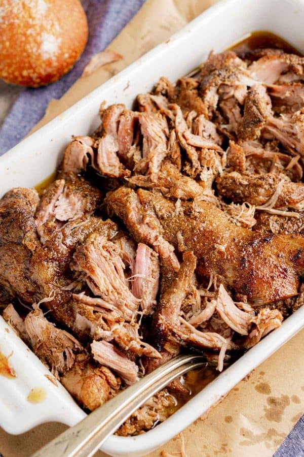 slow cooker pulled pork in white ceramic dish with forks