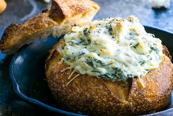 bread bowl of spinach artichoke dip in iron skillet on gray background