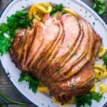 cooked spiral ham on serving platter garnished with parsley and orange slices