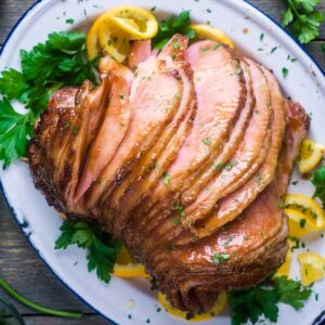 Orange glazed spiral ham on serving platter garnished with parsley and orange slices