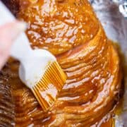 glaze is brushed over spiral ham in foil-lined roasting pan