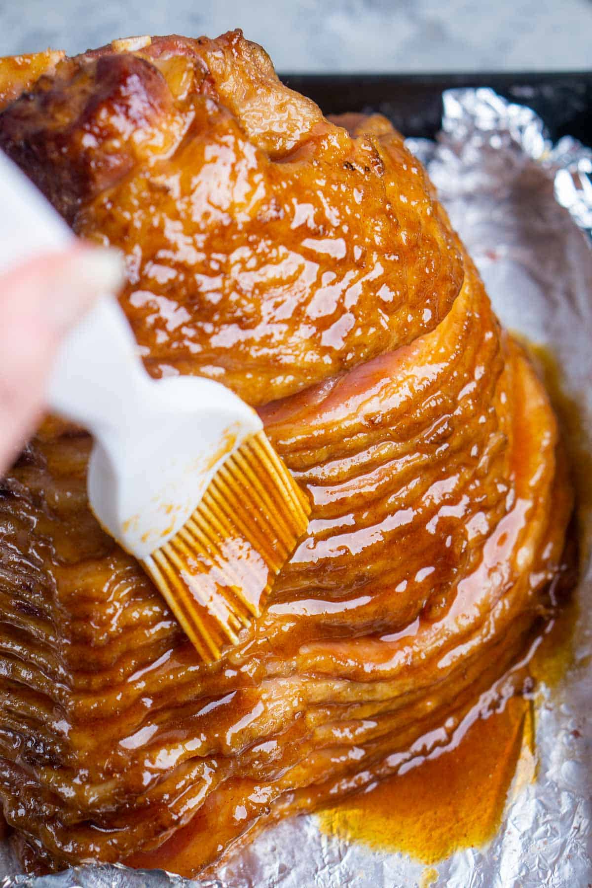 glaze is brushed over spiral ham in foil-lined roasting pan