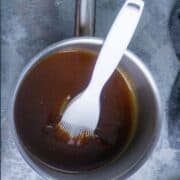 A saucepan filled with ham glaze and a white silicone basting brush resting inside on a gray surface.