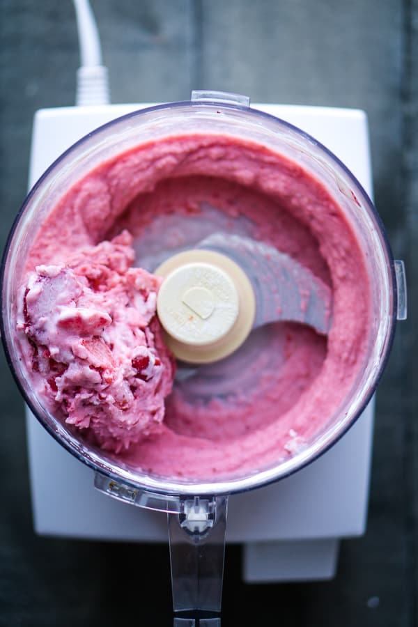 Strawberry frozen yogurt being blended in Cuisinart food processor on gray wood background