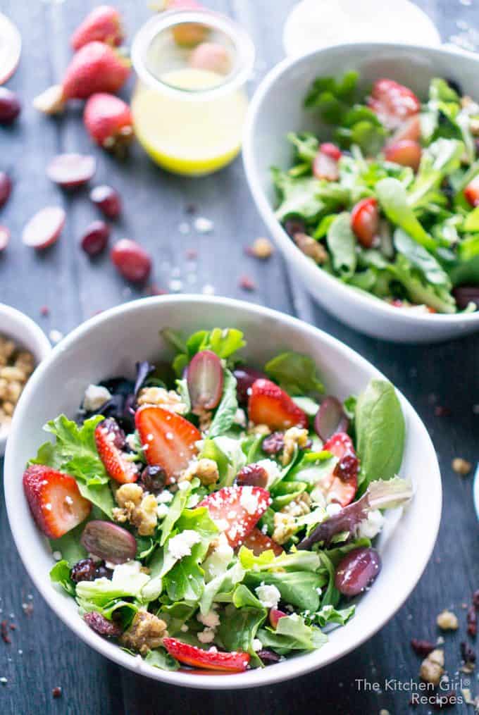 strawberry salad with spring mix in white bowl on grey wooden background with grapes and vinaigrette