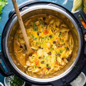 cheesy taco pasta in the Instant Pot on blue table with garnish and colorful napkin