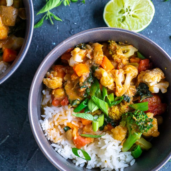 Vegetable curry with white rice in gray bowls on gray background with lime garnish