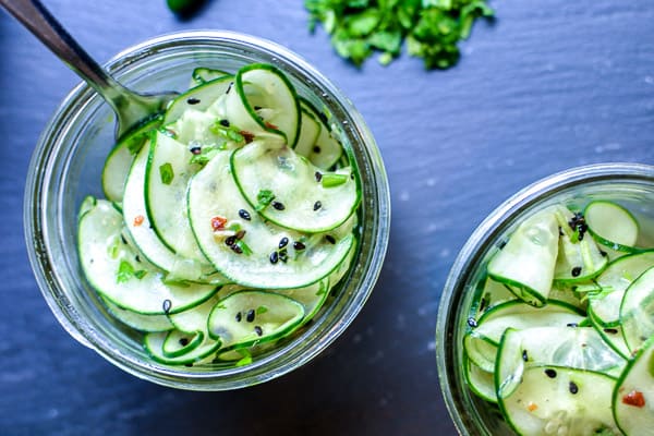 two Thai cucumber salads in mason jars with fork on black background