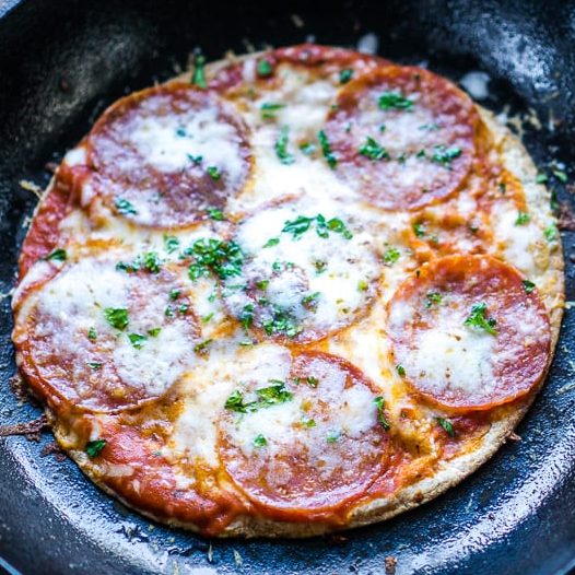 whole pepperoni tortilla pizza in iron skillet on brown wooden background