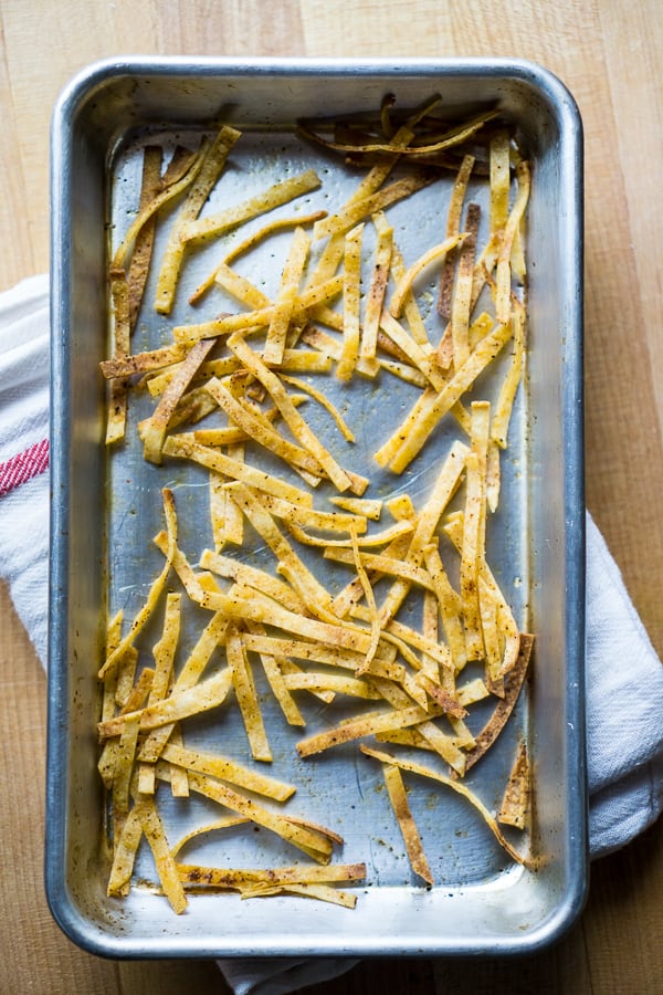 baked tortilla strips on baking sheet on white towel on wood surface