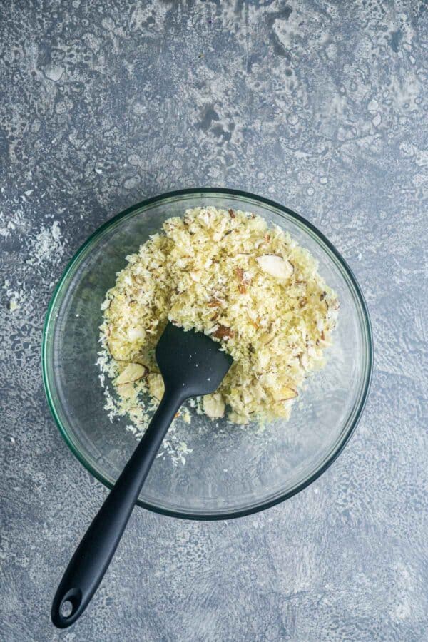 panko bread crumbs, sliced almonds, and olive oil are combined in a glass bowl with a black spatula