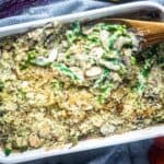 wooden spoon scoops creamy vegan green bean casserole from a white baking dish