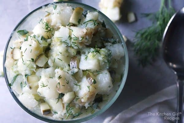vegan potato salad no mayo in glass bowl with fresh dill and chunks of potato scattered around the bowl