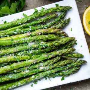 Closeup of asparagus on white platter garnished with parmesan and parsley