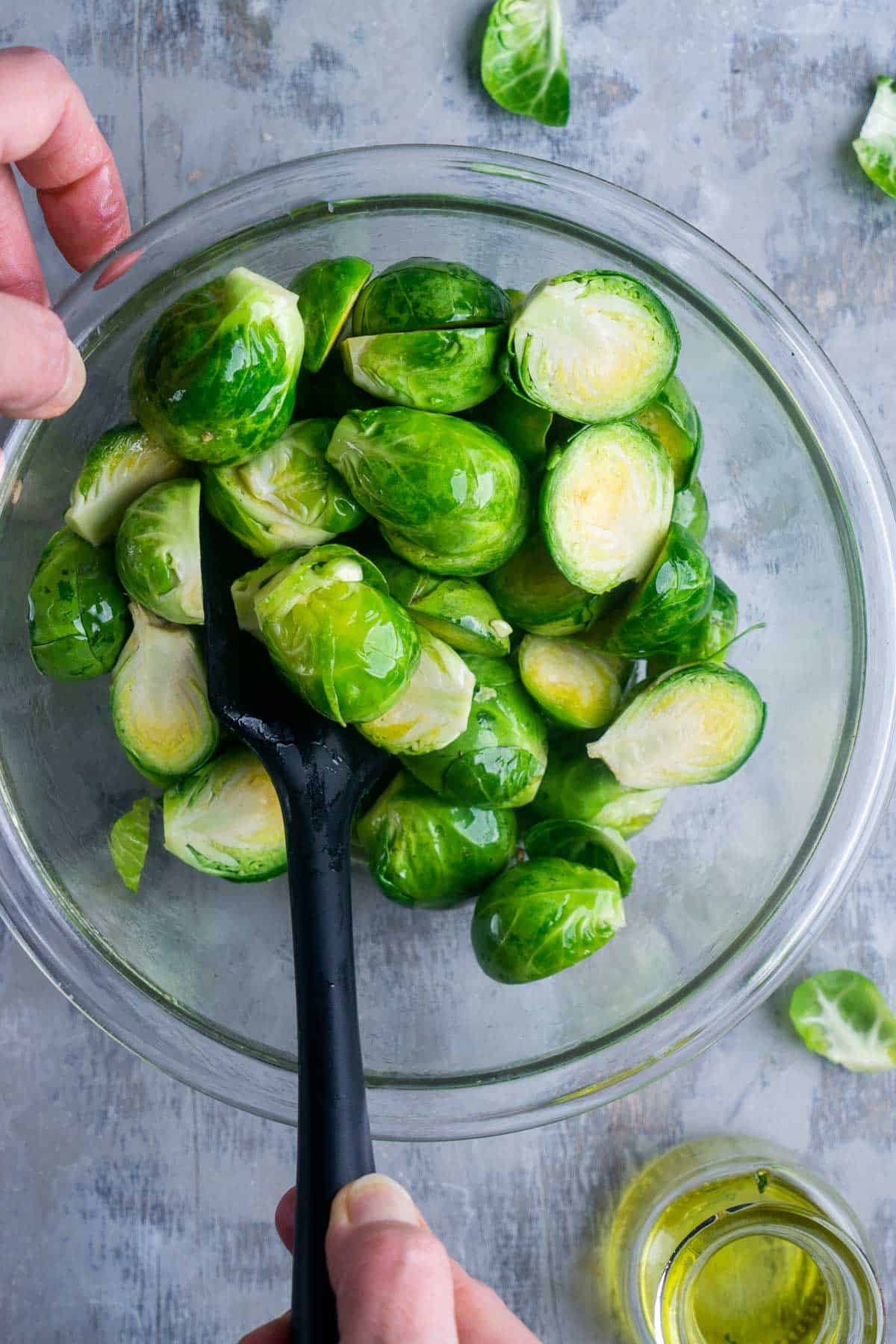 Tossing Brussels sprouts with oil in glass mixing bowl