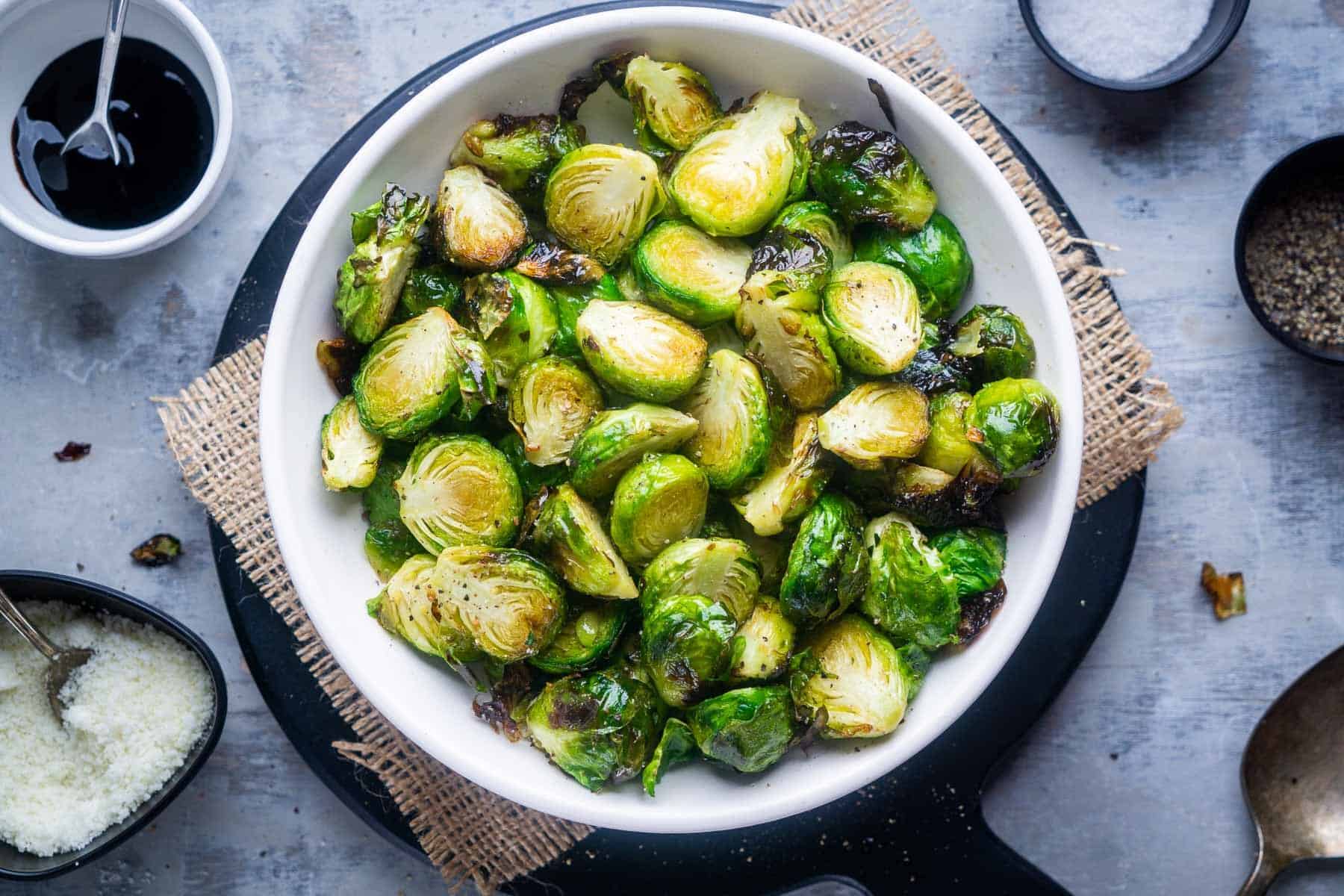 Air fryer Brussels sprouts in white serving bowl, with assorted garnishes