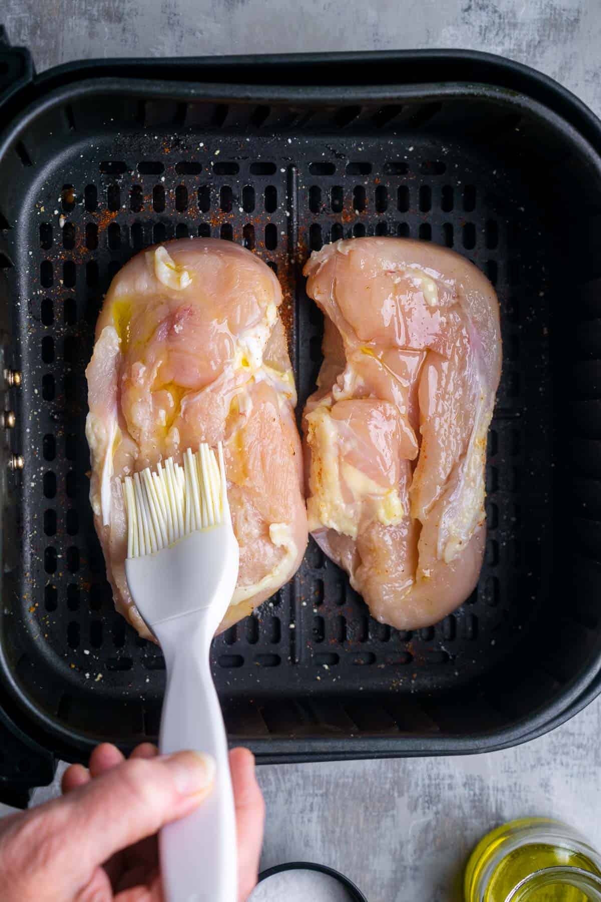 Brushing oil onto two chicken breasts in air fryer