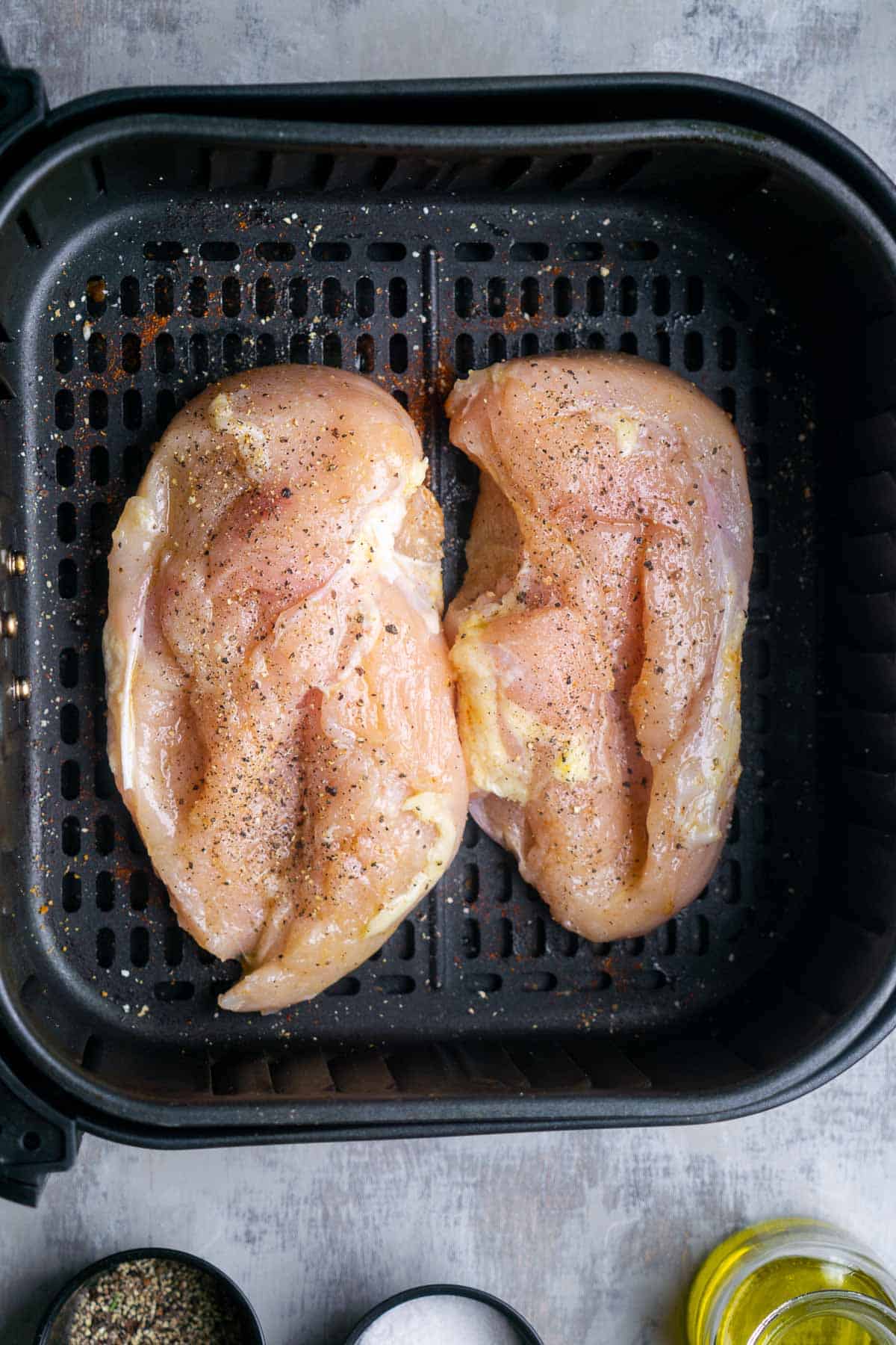 Two uncooked chicken breasts in air fryer basket