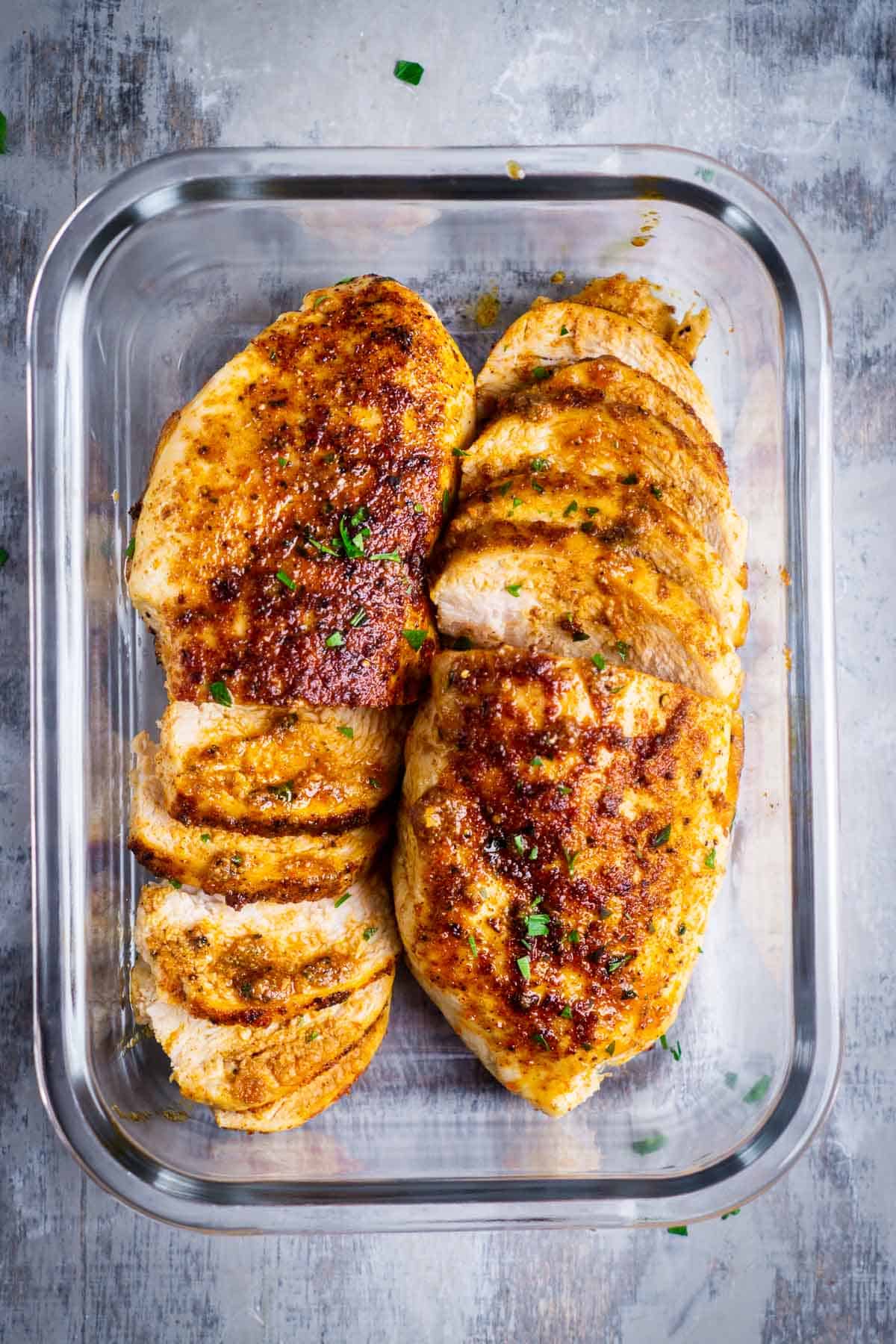 Two partially sliced chicken breasts in glass baking dish