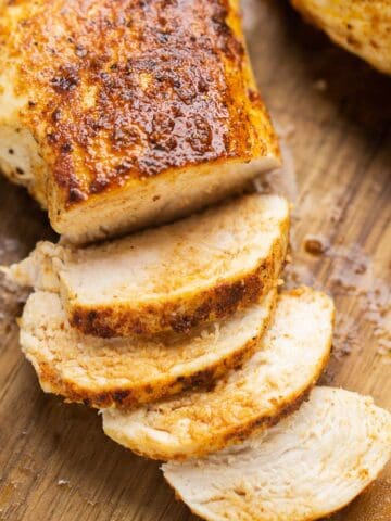 Partially sliced air fryer chicken breast on wooden cutting board