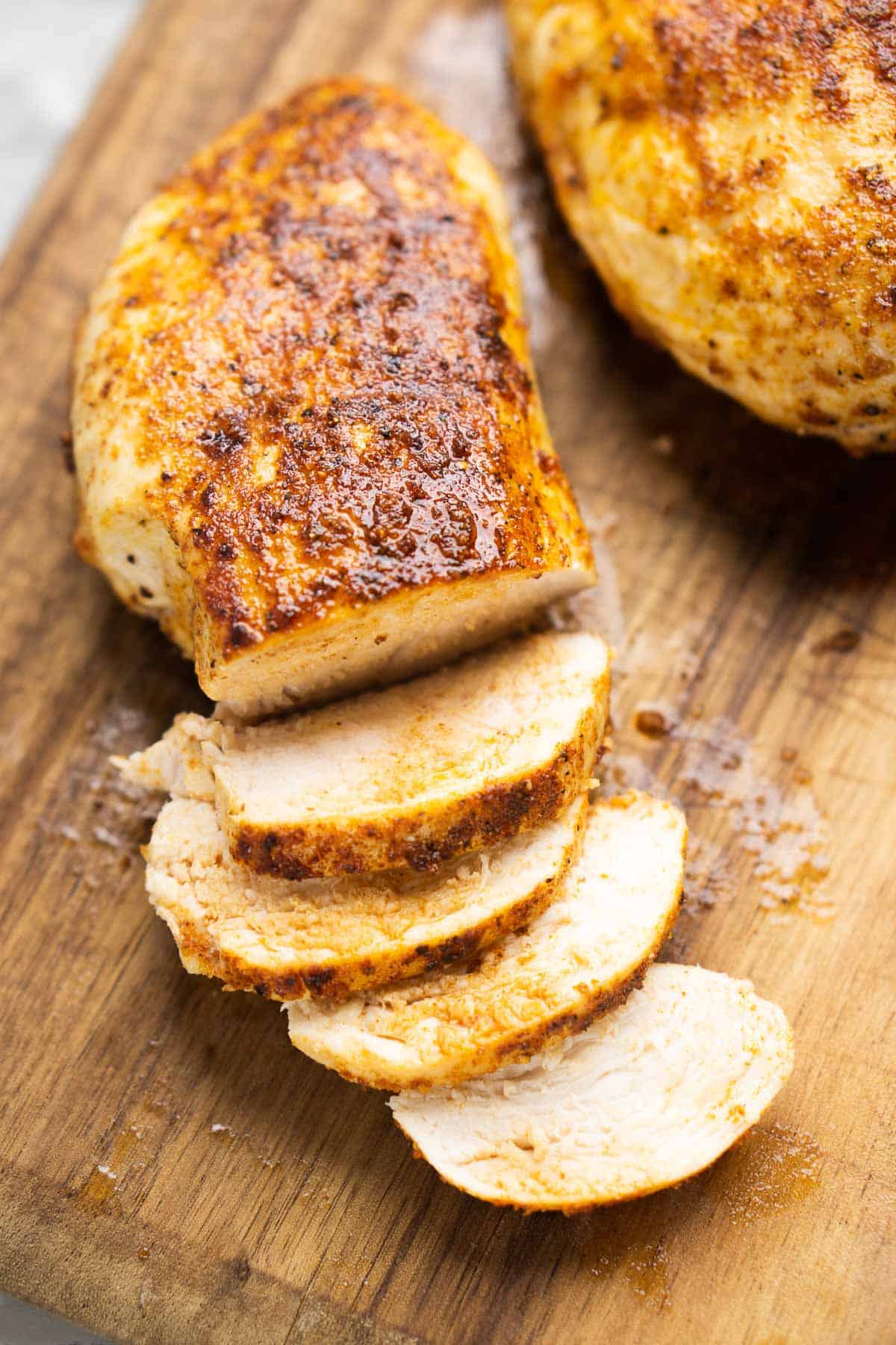 Partially sliced air fryer chicken breast on wooden cutting board