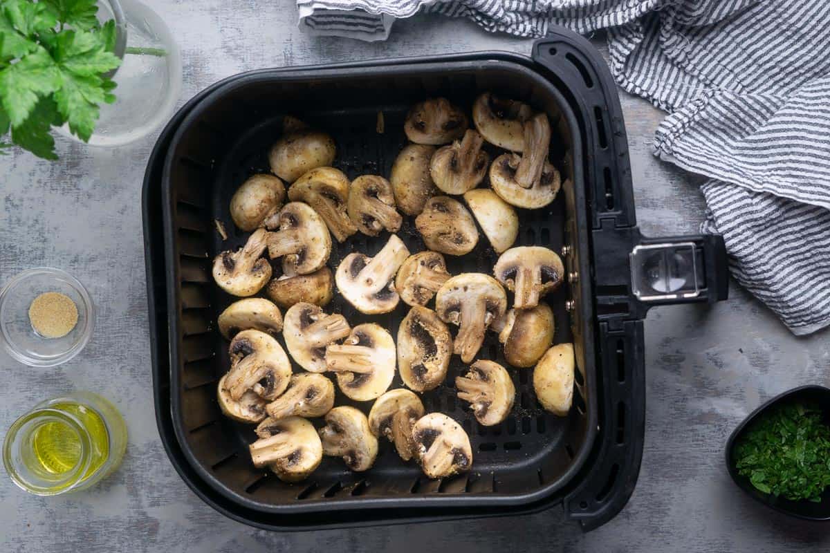mushrooms are spread out in air fryer basket before getting air fried