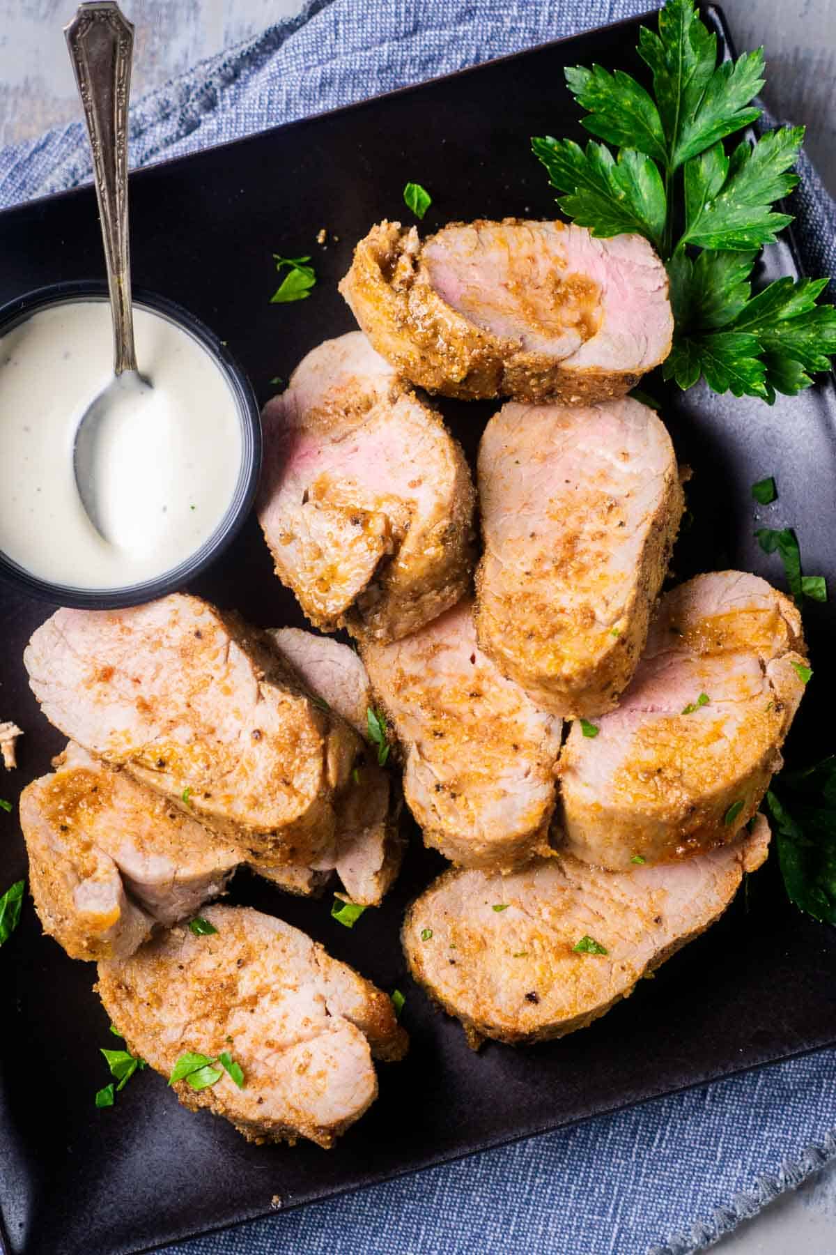 Sliced air fryer pork tenderloin on square plate with parsley and sauce