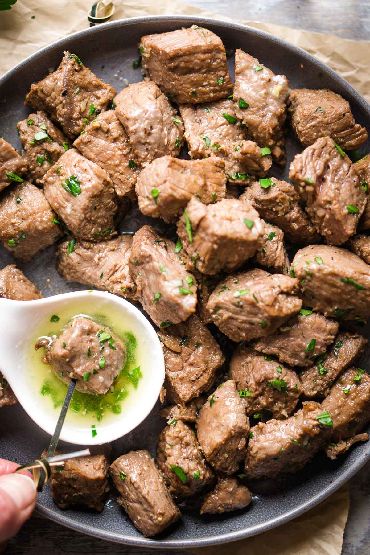 steak cube is dipped in garlic butter sauce on a platter of air fryer steak bites
