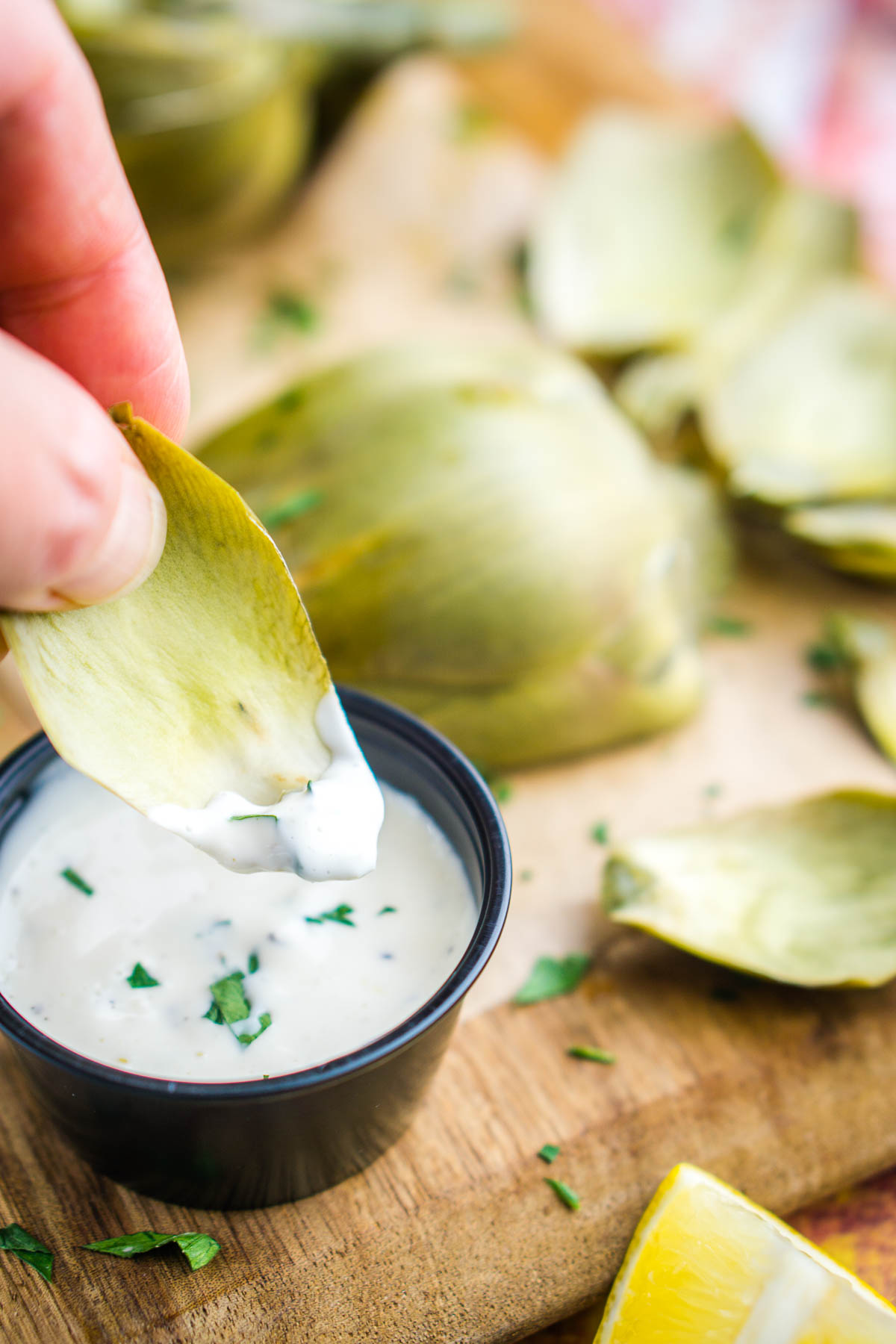 hand dips artichoke leaf in dipping sauce
