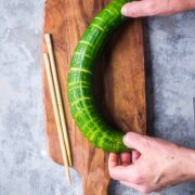hands holding cucumber by both ends, bending it to reveal the slicing results