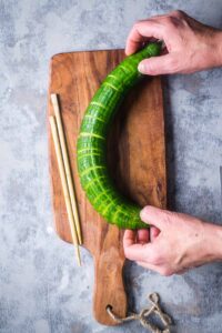 hands holding cucumber by both ends, bending it to reveal the slicing results