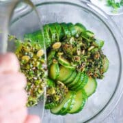 Asian dressing is poured over sliced cucumber in glass mixing bowl