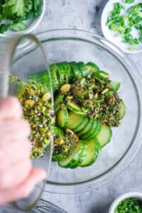 Asian dressing is poured over sliced cucumber in glass mixing bowl