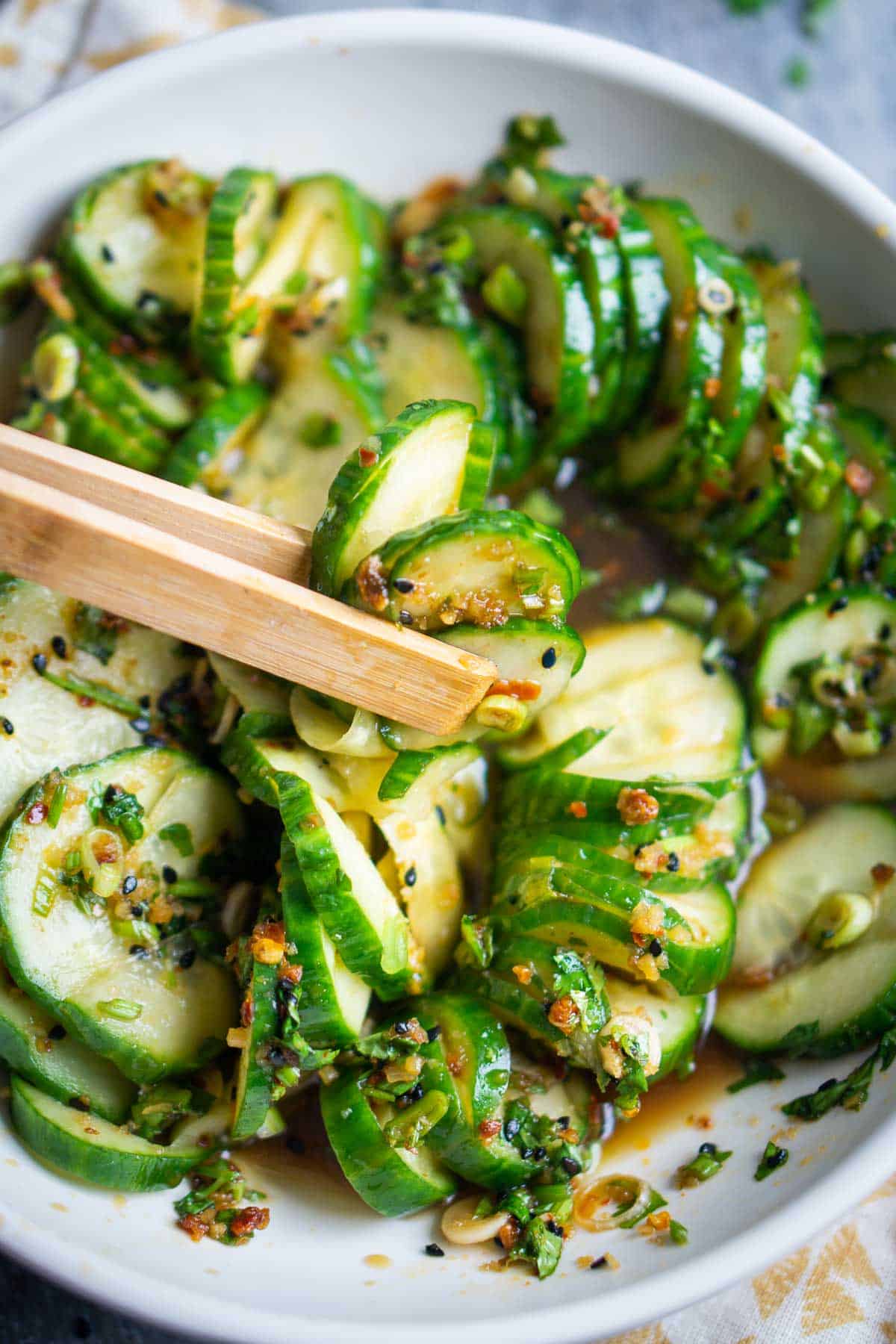 wooden tongs picking up Asian cucumber salad from white serving bowl