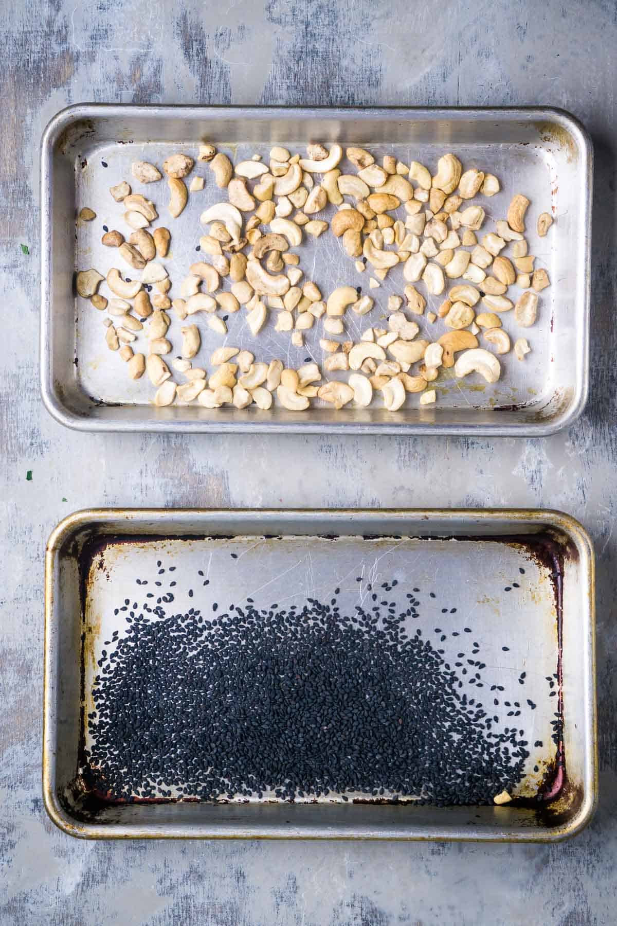 baking sheet with toasted cashews next to baking sheet with toasted black sesame seeds