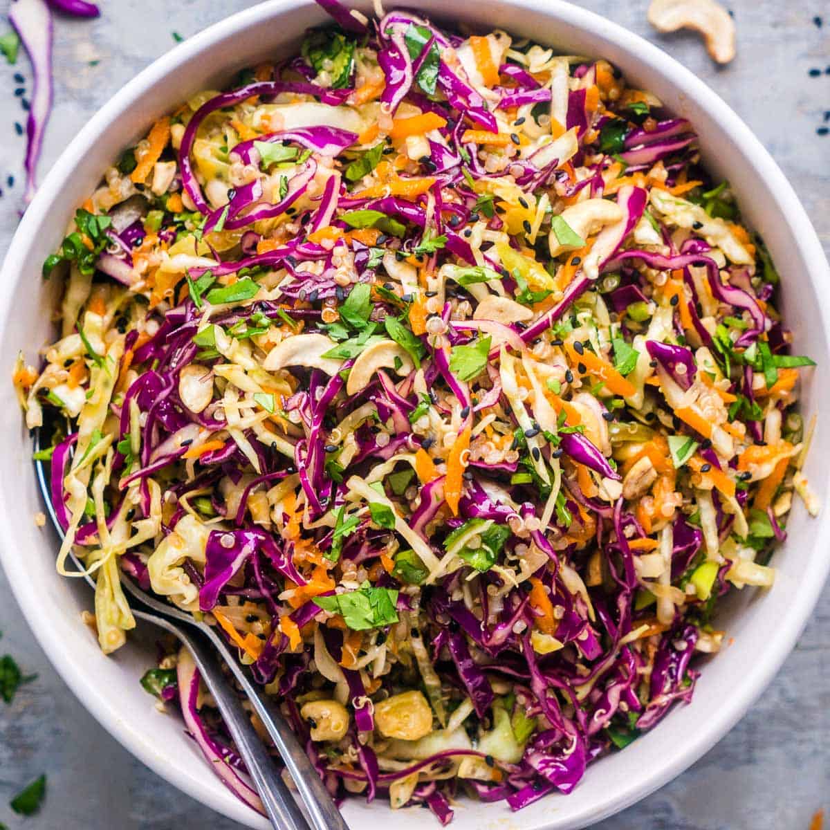 asian slaw in white bowl with two serving spoons